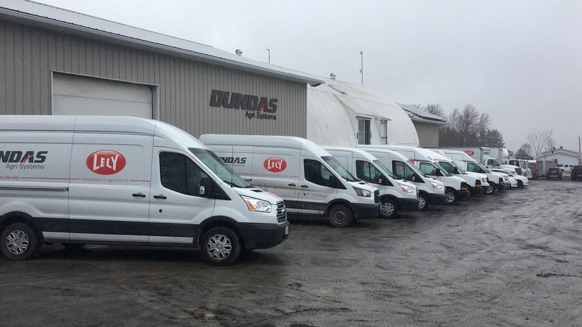 A fleet of white vans parked in a line outside industrial buildings, each with the logo 'DUNDAS AG Systems' and a smaller 'LEVY' logo, on an overcast day with wet ground.