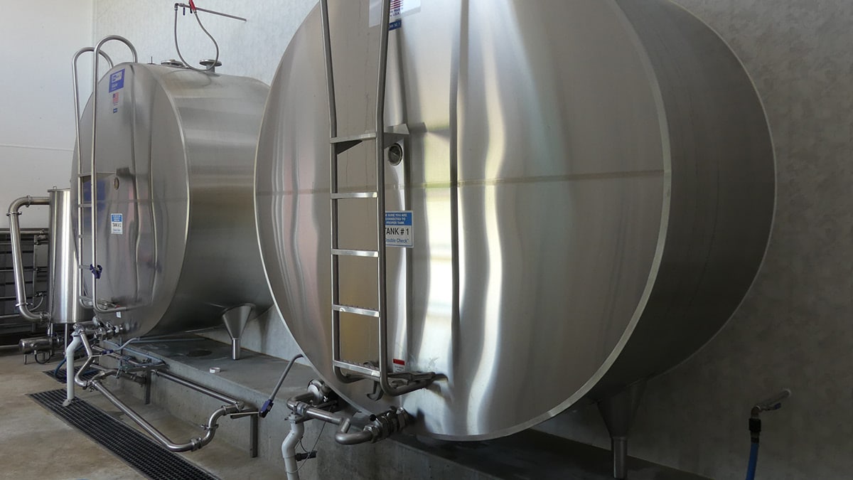 Two large stainless steel industrial tanks with conical bases, equipped with pipes and valves, used in processes like brewing, pharmaceuticals, or food production, showcasing industrial equipment and process engineering.