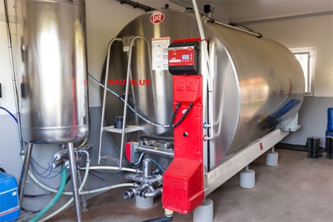 Large stainless steel tank with red machinery attached, located in an industrial or agricultural setting. The tank has several pipes and valves connected to it, with a control box labeled ‘NAUTILUS’ featuring dials and switches.