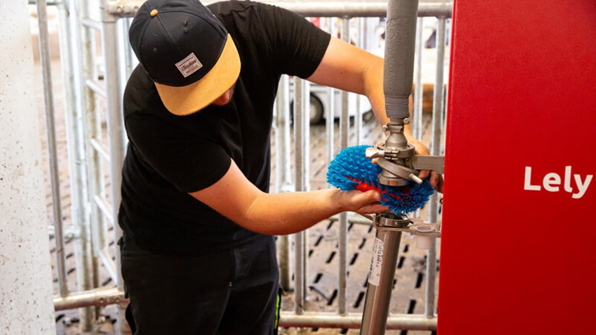 A guy with a hat and a black t-shirt repairing a Lely machine