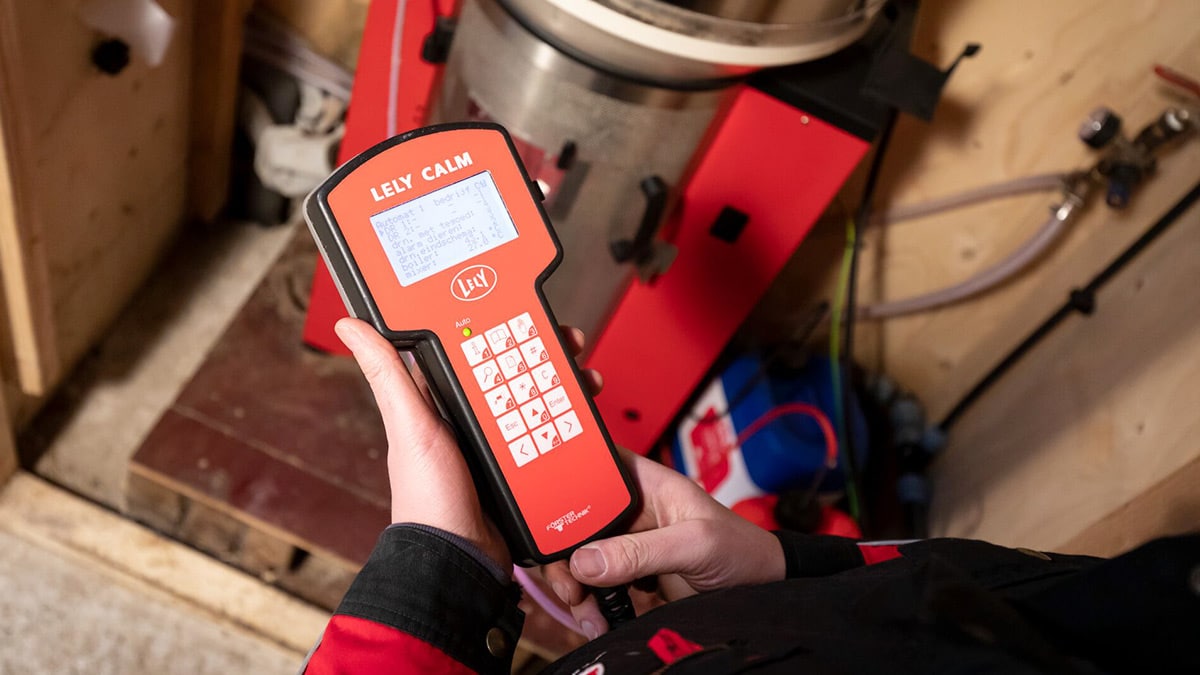 Person’s hand holding a red electronic measuring tool with a digital screen and keypad, used for maintenance or technical work.